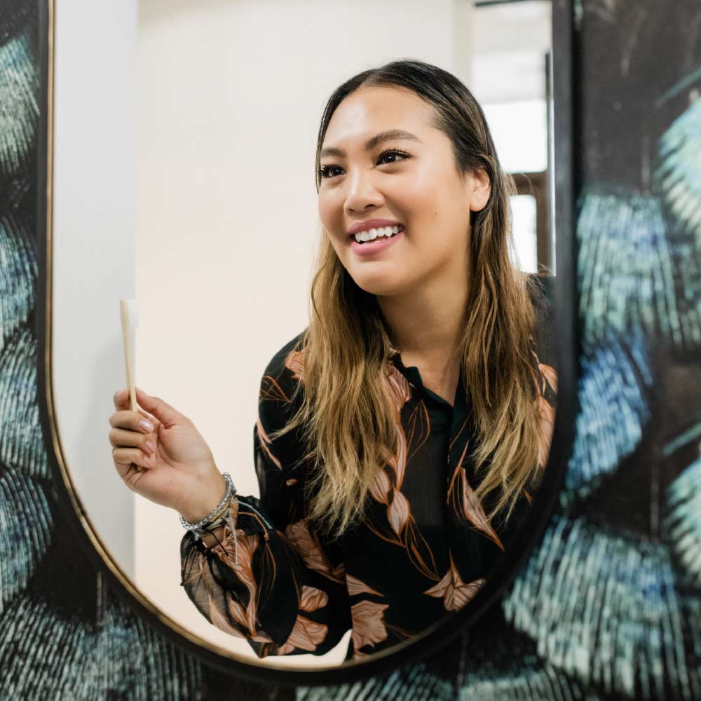 Photo of a smiling patient holding a toothbrush and looking at herself in the mirror